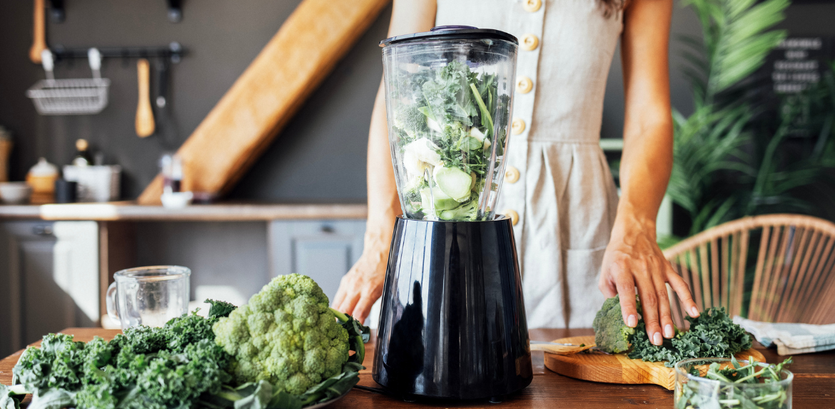 Close-up of a blender with green herbs and vegetables.
