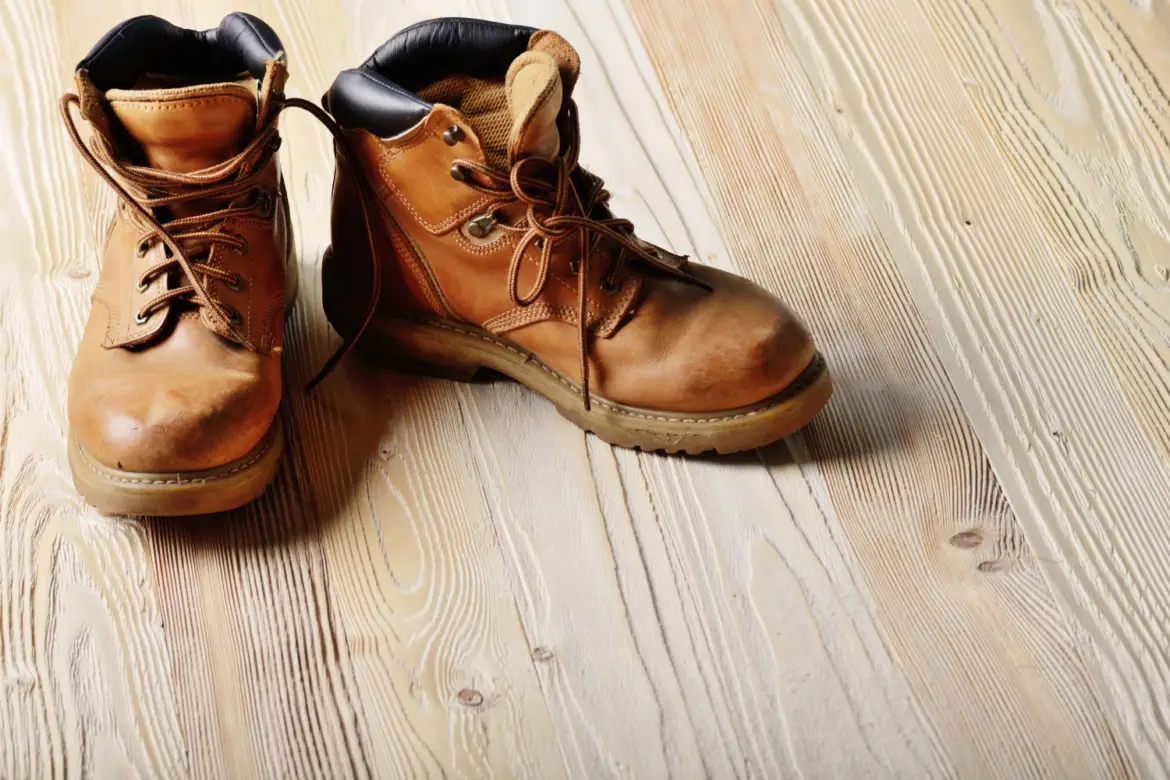 Yellow leather used work boots on wooden background closeup