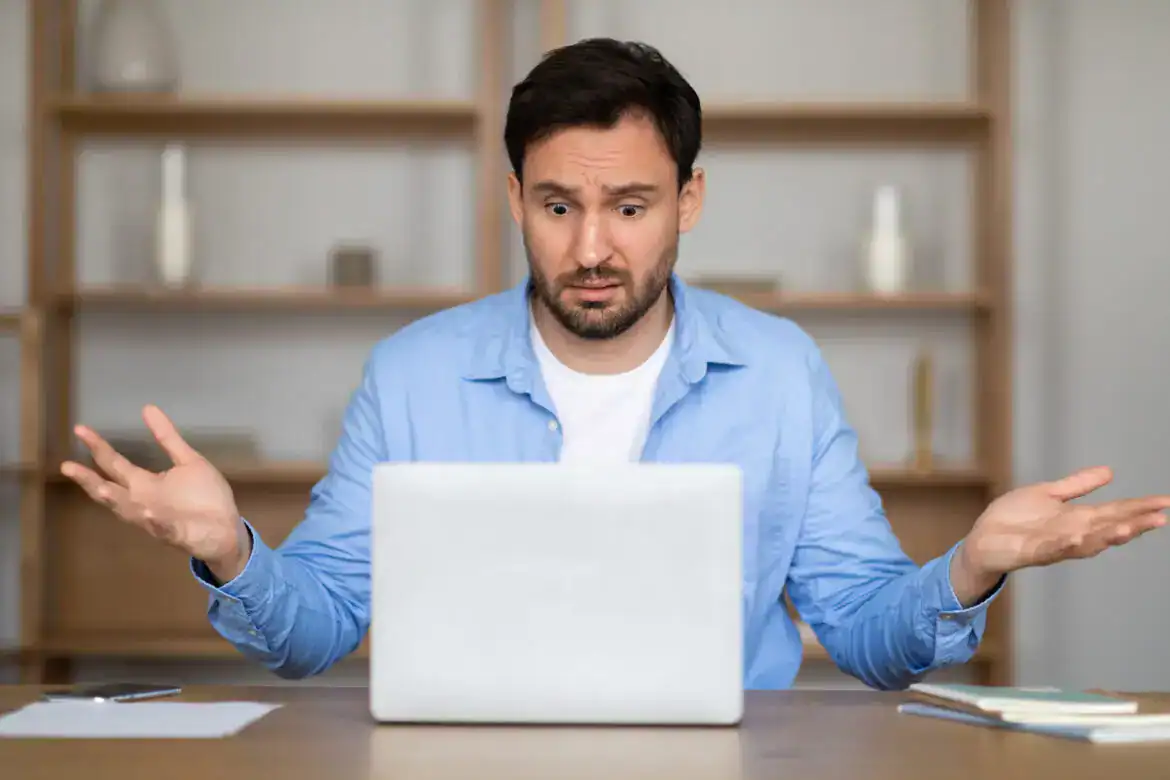 Frustrated Man in Blue Shirt Expressing Confusion at Laptop
